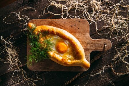 Top view on caucasian cuisine dish khachapuri in adjara with egg on the wooden board, horizontal