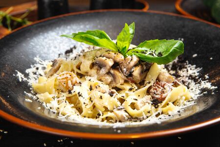 Closeup on appetizing tagliatelle alfredo pasta with mushroom and parmesan cheese in a dark plate, horizontalの写真素材