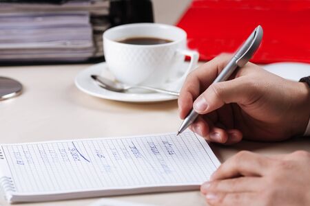 Working in office male hand writing in a notebook with a cup of coffee on the background, horizontalの写真素材
