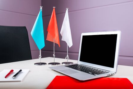 Light bright office workplace with a silver laptop, notebook, pens and different flags on the table, horizontalの写真素材