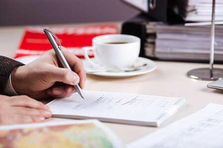 Working in office male hand writing in a notebook with a cup of coffee on the background, horizontal