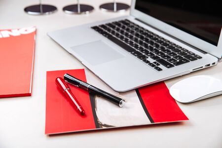 Office workplace with a silver laptop, papers and reports, pen, mouse on the table, horizontal, red colourの写真素材