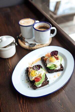 Top view on breakfast rye toast with avocado poched egg and salmon with coffee, vertical