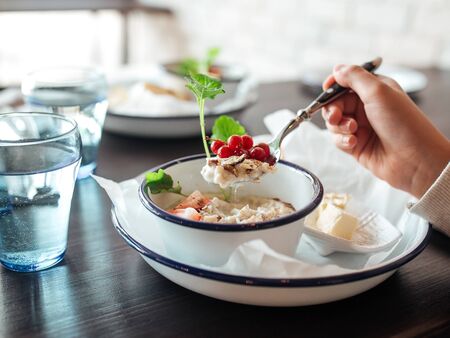 Hands eating morning healthy breakfast rice porridge with nuts and berries with glass of water,...