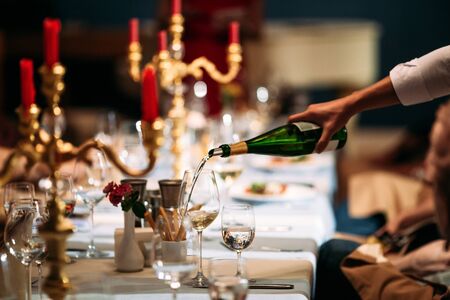 Waiter hand pouring wine in a glass on the served banquet restaurant table, horizontal