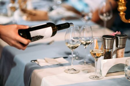 Waiter hand pouring wine in a glass on the served banquet restaurant table, horizontalの写真素材