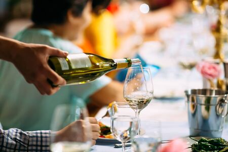 Waiter hand pouring wine in a glass on the served banquet restaurant table, horizontal