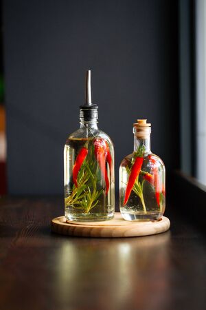 Closeup on glass jars with vinegar sauce with pepper and rosemary on the dark wooden table, vertical