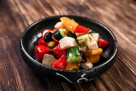 Closeup on fresh healthy greek salad with vegetables olives and cheese in a black bowl on the wooden table, horizontalの写真素材