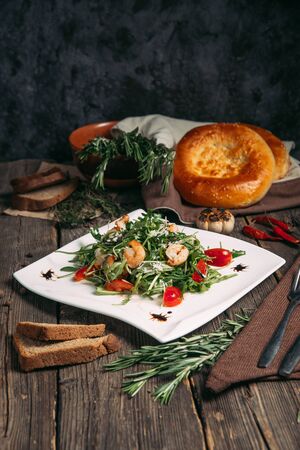 Side view on arugula shrimps and tomatoes salad on a white plate, verticalの写真素材