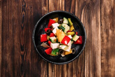 Top view on fresh healthy greek salad with vegetables olives and cheese in a black bowl on the wooden table, horizontalの写真素材