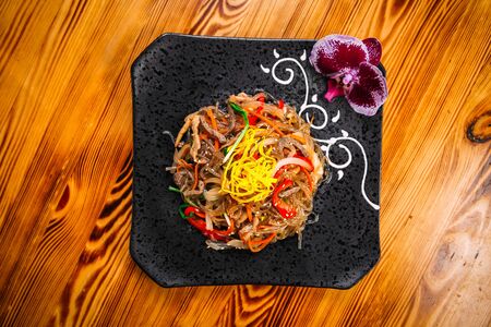 Top view on appetizing asian dish funchoza noodles with beef and vegetables on a black plate,...