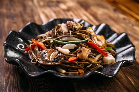 Closeup on seafood soba noodles wok in a black plate, horizontal