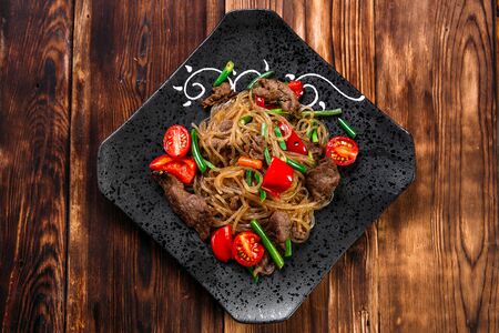 Top view on appetizing asian dish funchoza noodles with beef and vegetables on a black plate, horizontalの写真素材