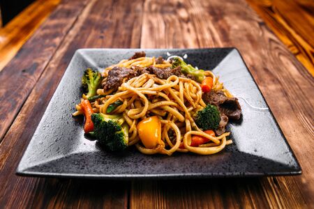 Closeup on asian cuisine beef and vegetables udon noodles wok on the wooden table, horizontalの写真素材