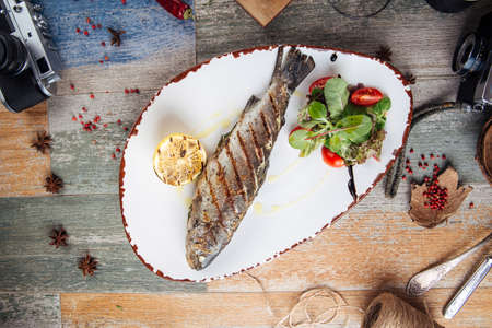 Top view on grilled trout fish with salad and lemon on the wodoen table, horizontalの写真素材
