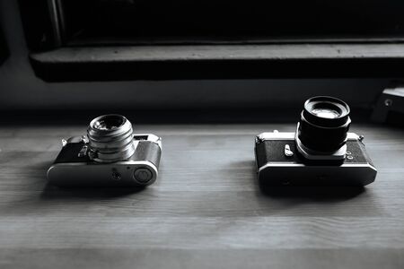 Two retro film cameras lie on a wooden table. Black and white. Horizontal