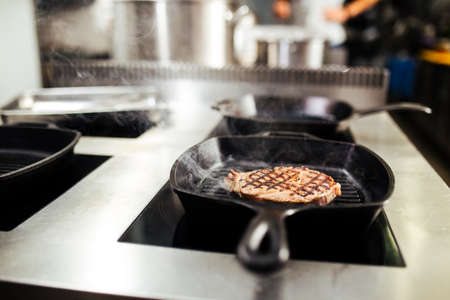 Cooking beef steak on a black grill pan in restaurant kitchen, horizontalの写真素材