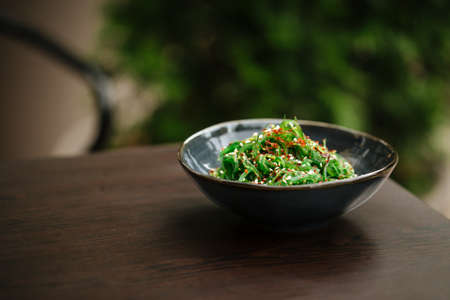 Green chuka seaweed salad in a black bowl on the wooden table with blurry background