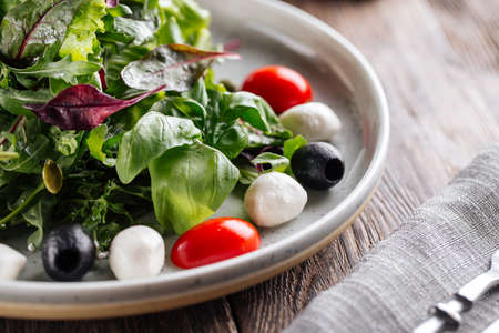 Closeup on fresh salad with greens mozzarella olives and tomatoes