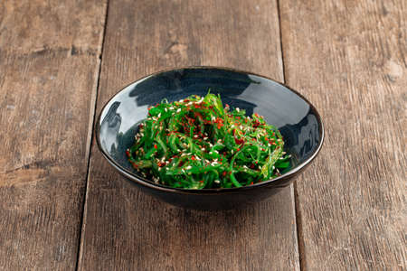 Green chuka seaweed salad in a black bowl on the wooden tableの写真素材