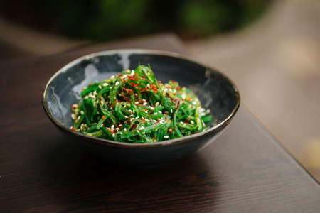 Green chuka seaweed salad in a black bowl on the wooden table with blurry background
