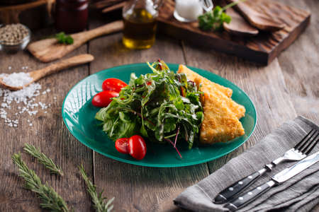 Fried cheese with green and tomatoes salad on the wodoen tableの写真素材