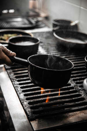 Chef cooking food in a black pan on a fire in the restaurant kitchenの写真素材