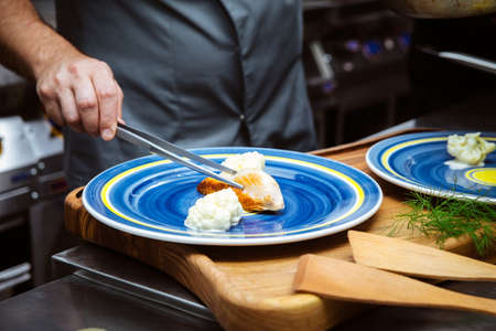 Italian restaurant chef preparing chicken with soft cheese and dill on a blue plate on the tableの写真素材