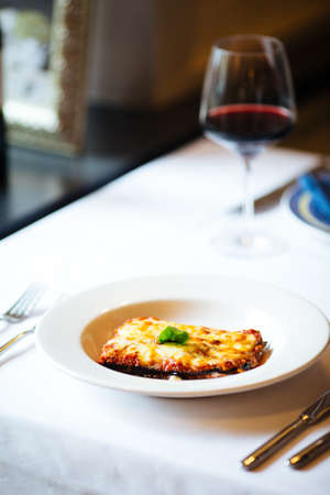 Italian cuisine dish parmisan eggplant with a glass of red wine on the white plate on the white tableの写真素材
