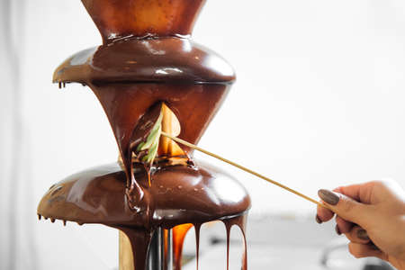 Woman hand using a chocolate fountain with apple slices on a skewerの写真素材