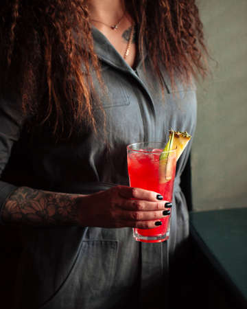 Woman holding red cocktail in a highball with ice and pineappleの写真素材