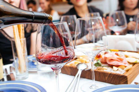Pouring red wine in a glass in restaurant with appetizersの写真素材