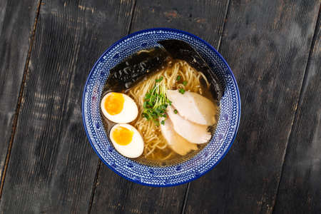 Top view on asian japanese shio ramen noodle soup with pickled agitama egg and chicken breast on the dark wooden tableの写真素材