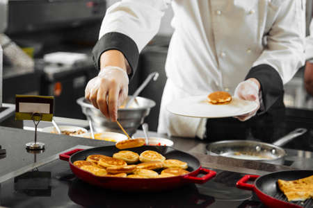 Chef puts pancakes on a plate from pan on the restaurant kitchenの写真素材