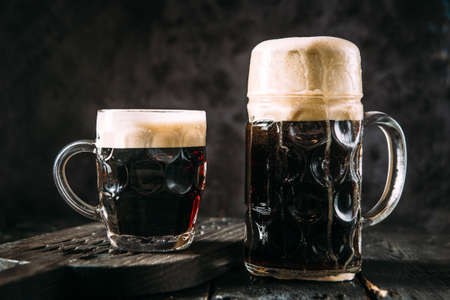 Two glass mugs with dark beer on the black background