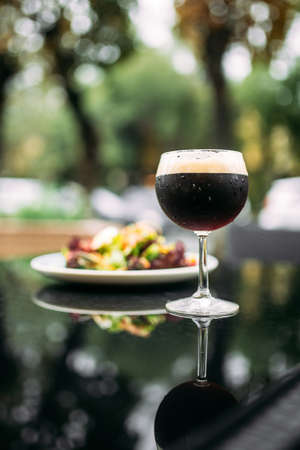 Dark draft beer in a glass with a dish on the glass table outdoorの写真素材