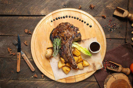 Top view on cowboy beef steak on a wooden board with potatoesの写真素材