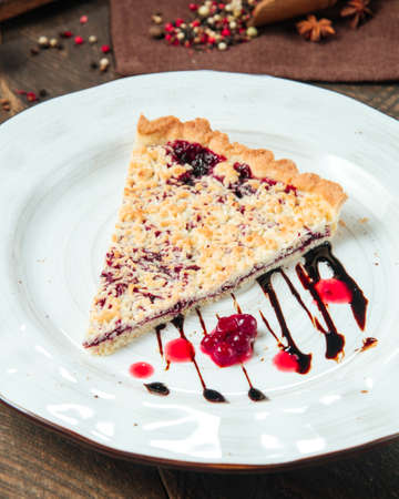 Closeup on berry pie decorated with chocolate sauce on the white plate on the wooden table