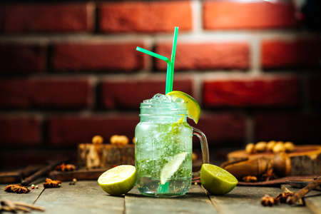 Side view on lime lemonade in a glass mug with brick wall on the background