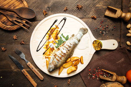 Top view on grilled fish with potatoes served on the wooden board
