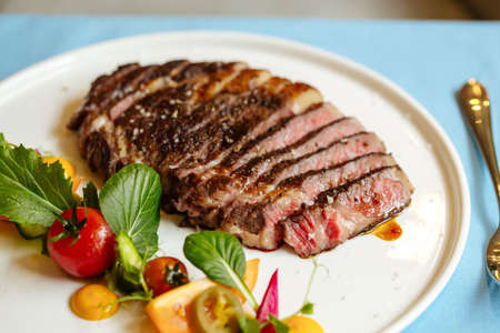 Closeup on sliced ribeye beef steak with fresh vegetable salad on the blue tableの写真素材