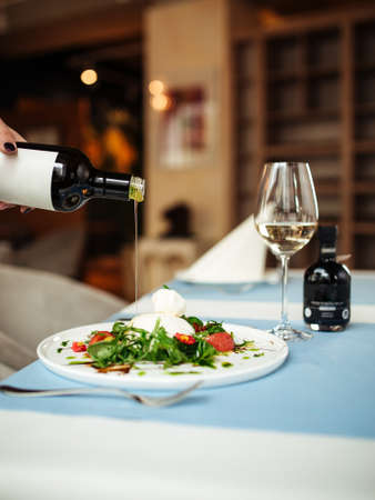 Pouring oil on spanish buratta salad on the restaurant tableの写真素材