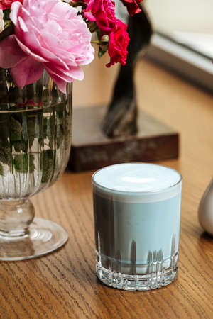 Blue lavander latte beverage in a glass on the table with flowersの写真素材