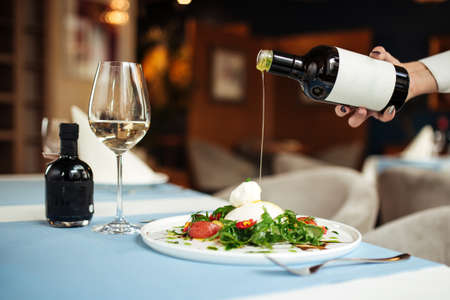 Pouring oil on spanish buratta salad on the restaurant table