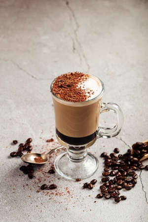 Mocaccino coffee in a glass mug on the grey concrete background decorated with beans