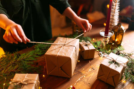Female hands tying holiday craft gift box with spruce branches on the wooden tableの写真素材