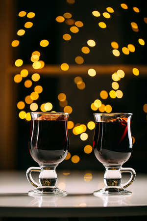 Side view on two glass mugs of glintwine with blurry lights on the background
