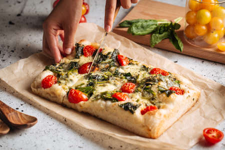 Hand slicing italian bread focaccia with spinachの写真素材