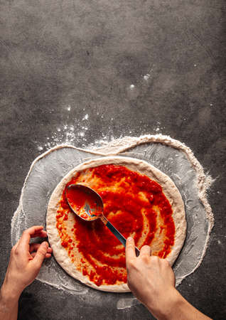 Making a pizza spreding tomato sauce on the doughの写真素材